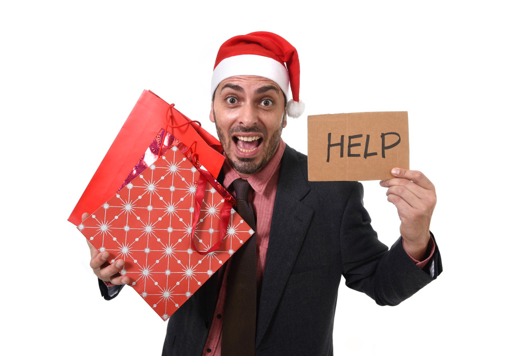 businessman in Santa Claus Christmas hat holding shopping bags help sign overwhelmed tired and  in stress