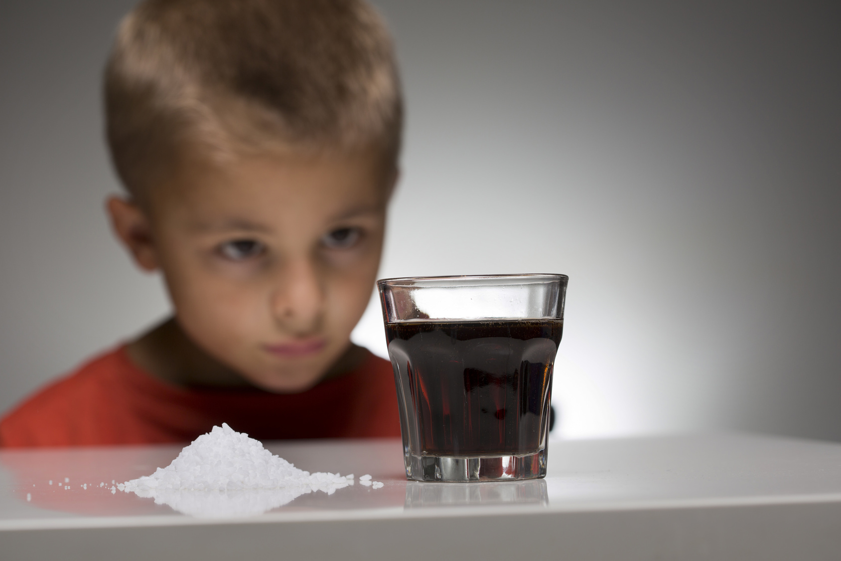 Concept photo of a child in front of a soft drink with sugar. The over-consumption of sugar-sweetened soft drinks is associated with obesity, type 2 diabetes, dental caries, and low nutrient levels.